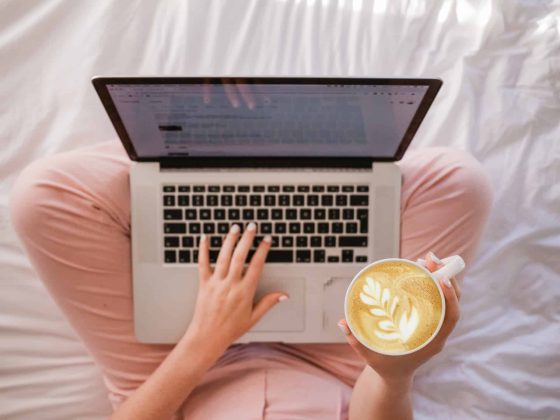 woman in pink pj bottoms typing on a laptop on a white bed sheet illustrating the acupuncture for fertility Chantal Nogbou article on best fertility now