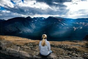 blond haired woman with her back to us sitting on a wall overlooking a vast dark blue mountain, illustrating the self love for valentines day artilce at best fertility now