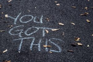 tarmac ground with leaves scattered across it with the words you got this written in white chalk, illustrating self love