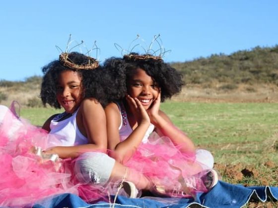 twin black girls, smileing in pink tutu's, on a green hillside, the twins are wearing brown twisted twig crowns, illustration best fertility now ivf twins article