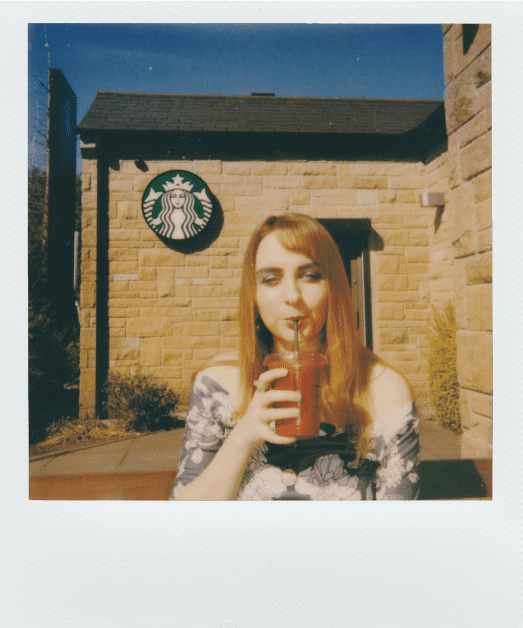 woman holding an iced coffee infront of a starbucks shop illustrating caffeine causing miscarriages
