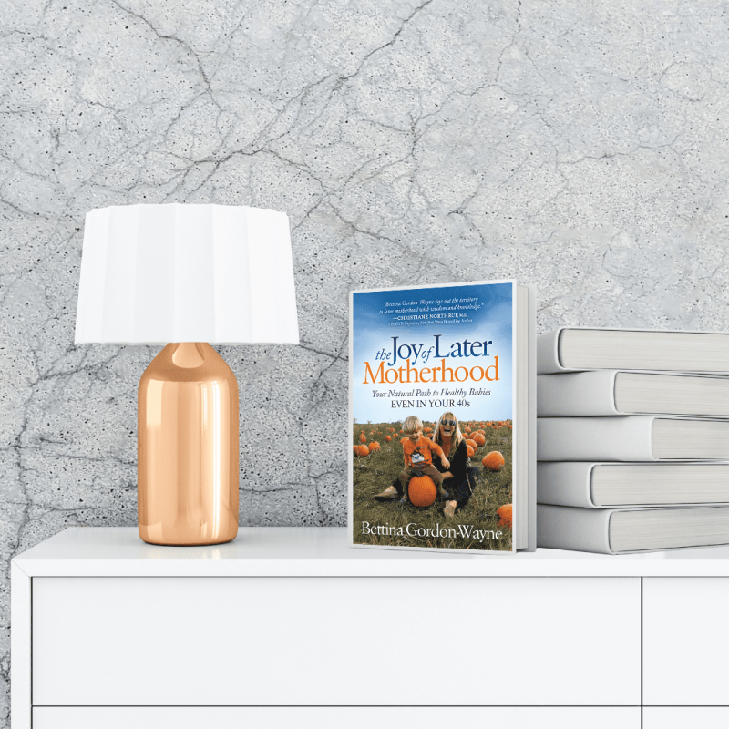 The Joy of Later Motherhood: Your Natural Path to Healthy Babies Even in Your 40’s book on a white chest of draws and a gold lamp to the left with a white lampshade