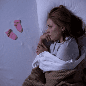 woman laying in bed crying over pink baby socks next to her illusration of the pain of words and how they can hurt miscarriage
