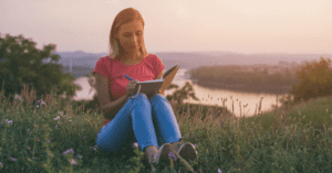 white woman with blonde hair in a medow wearing blue jeans and a pink towriting a letter illustrating the article Dear Future Egg Donor Mama