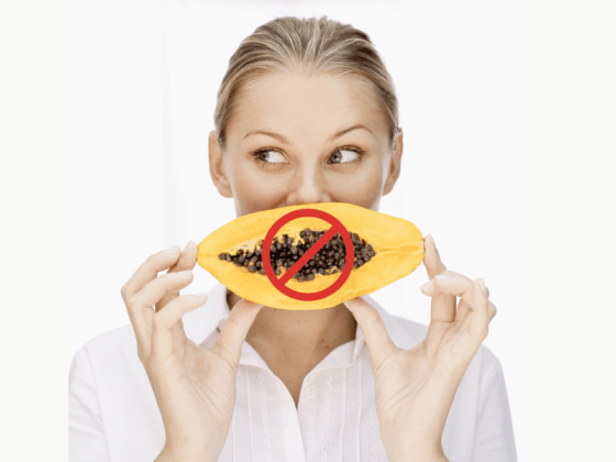 white woman on a plain background holing a papaya infront of her mouth, there is a red do not eat circle over the papaya illustrating the do not eat papaya for fertility reasons