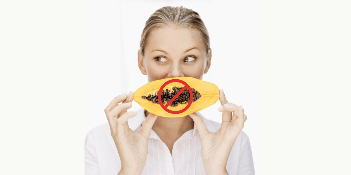 white woman on a plain background holing a papaya infront of her mouth, there is a red do not eat circle over the papaya illustrating the do not eat papaya for fertility reasons